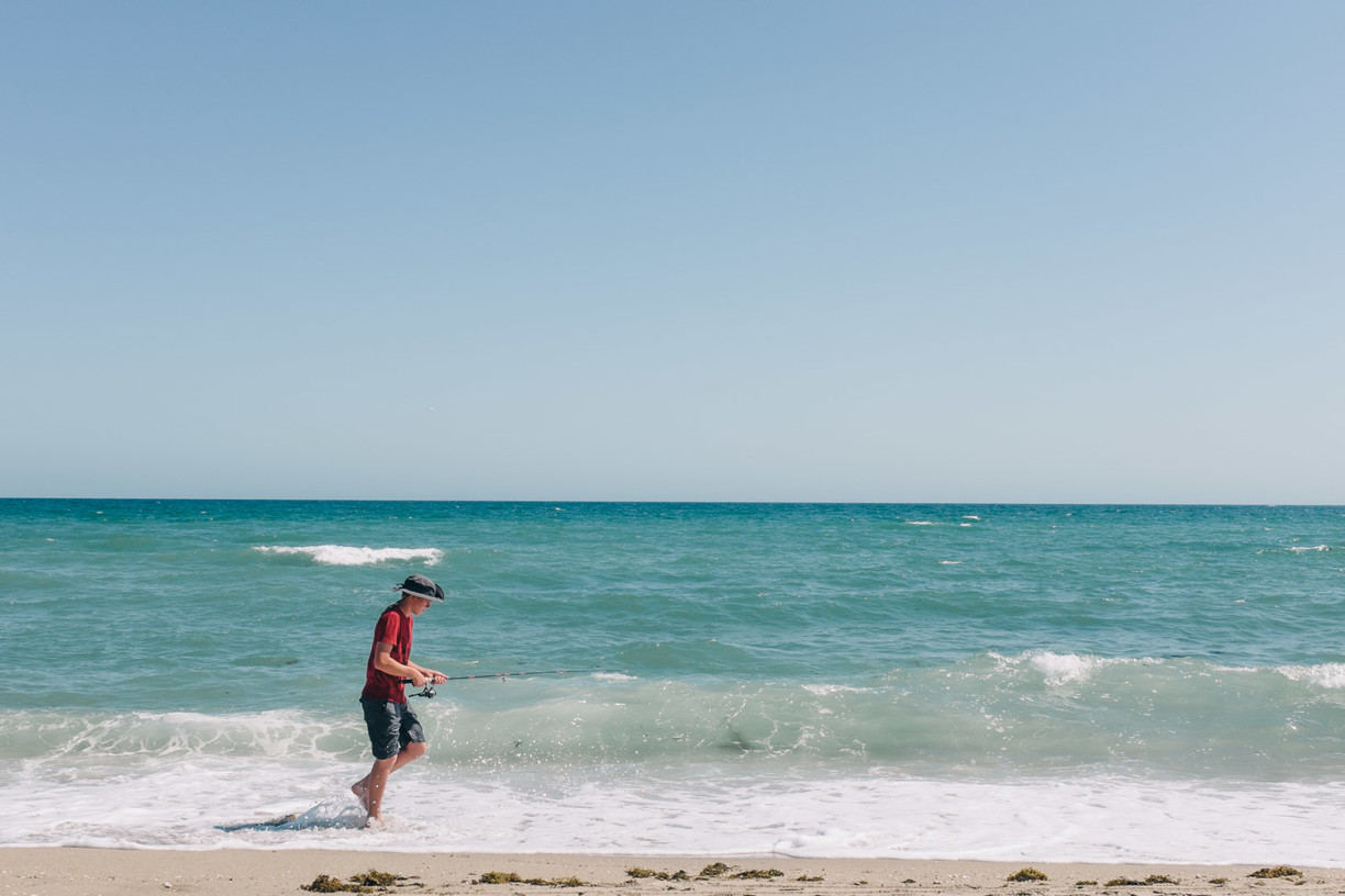 Young man walking with fishing rod in surf